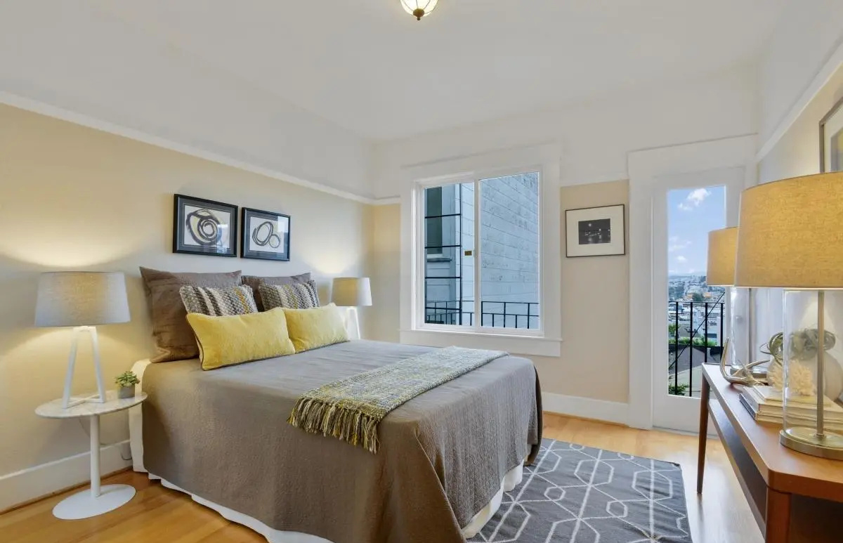 Guest bedroom with warm neutral palette, layered bedding, and city view window in a Lower Haight condo renovation.