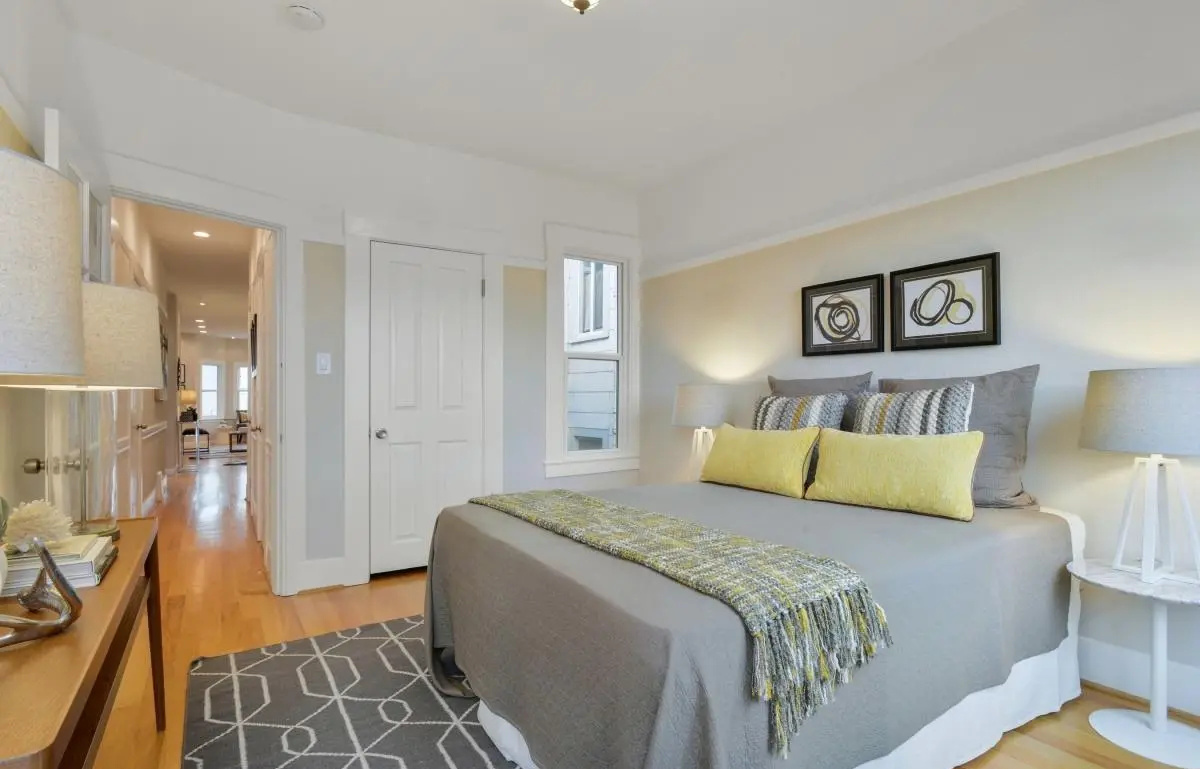Cozy guest bedroom with modern lighting, soft tones, and a view toward the open-concept living area in a Lower Haight Edwardian renovation.
