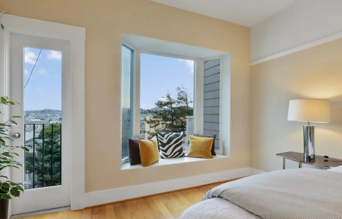 Bay window seating nook with accent pillows and city view in a renovated Edwardian bedroom, Lower Haight, San Francisco.