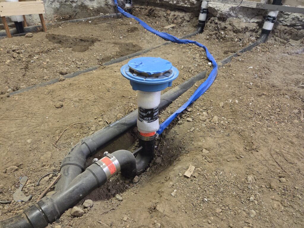 Horizontal vented ABS floor drain with trap primer line in groundwork plumbing installation.