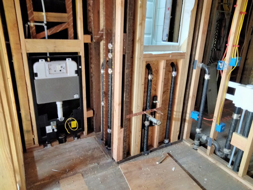 Powder room top-out with wall-hung WC carrier, cast iron DWV, and PEX supply lines in Bay Area home.