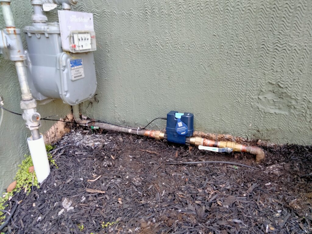 Exterior Moen Flo smart shutoff device installed on outdoor copper water main beside gas meter in San Francisco home.